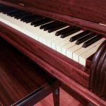 Close-up of an antique piano with reddish wood finish